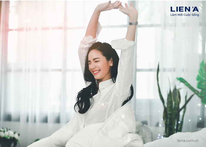 Người phụ nữ thức dậy với một nụ cười rạng rỡ, minh họa cho sự tỉnh táo và tràn đầy năng lượng sau một giấc ngủ ngon, thể hiện lợi ích của việc dậy sớm và ngủ đủ giấc mà tic.edu.vn luôn khuyến khích.